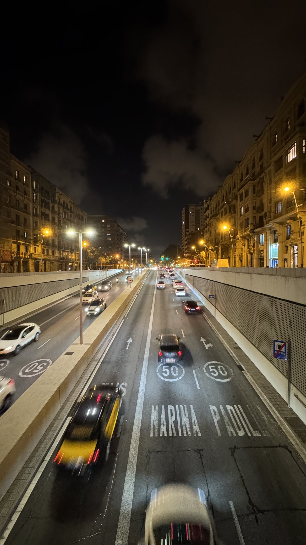 City avenue at night from above — light trails, taxis, lit apartment blocks